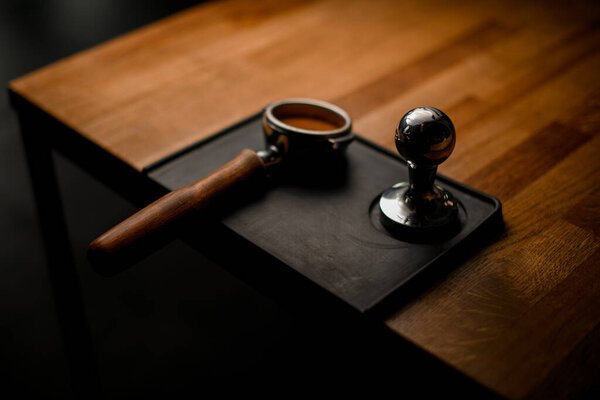 portafilter with tamped coffee and temper lying on black stand on wooden table