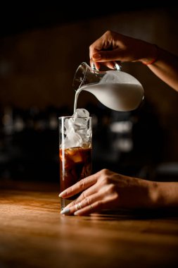 Kadınların elleri sürahiyi tutar ve bardağa buzlu kahve döker.