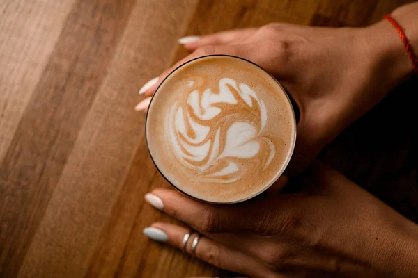 Bardağın üst görüntüsü, kadın ellerinde kahve içeceği. Köpük üzerindeki güzel desen — Stok fotoğraf