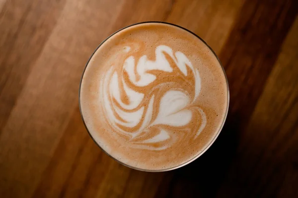 Vue du dessus du verre de café chaud avec belle latte art sur fond de table en bois. — Photo
