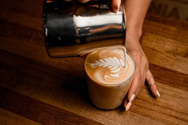 Close-up view of woman barista drawing pattern pouring milk into glass with latte — Stock Photo, Image
