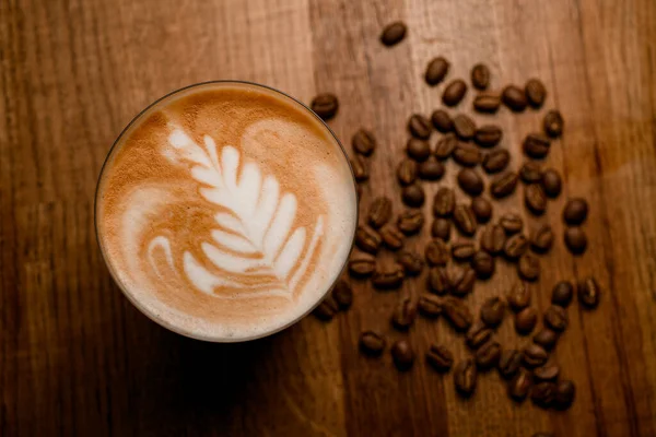 Vue de dessus du magnifique latte mousseux en verre et grains de café sur table en bois — Photo