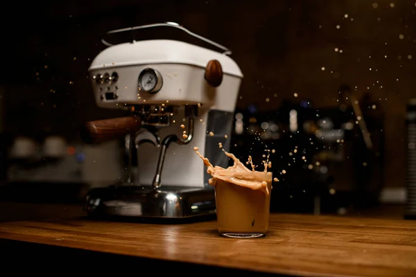 Masanın üzerinde köpüklü kakao içeceği olan bardak duruyor. Arka planda bulanık kahve makinesi — Stok fotoğraf