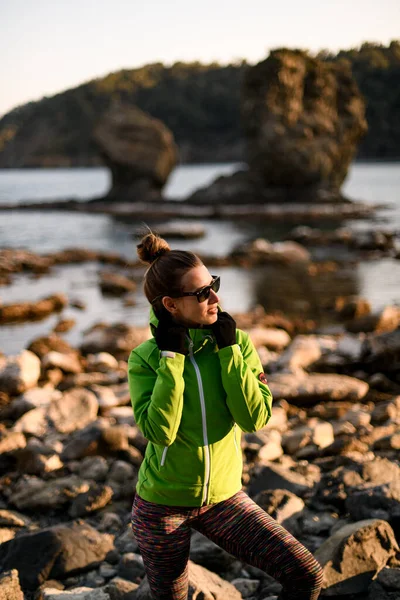 View of handsome young woman standing on the rocky coast of the sea — Stockfoto
