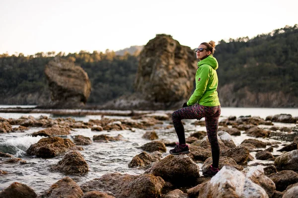 Hermosa vista de la atractiva joven mujer de los deportes de pie sobre piedra grande en la costa del mar — Foto de Stock