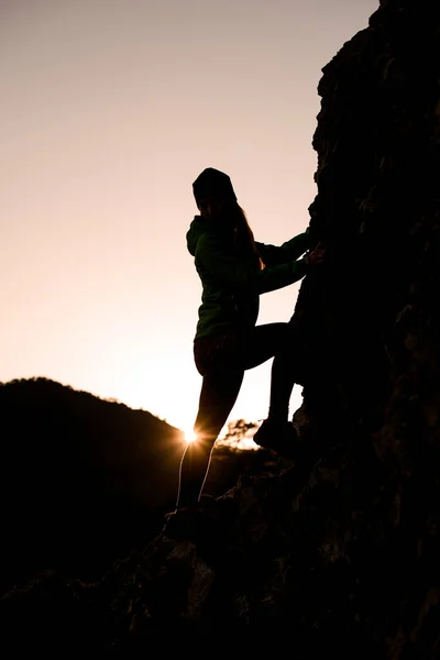 Силуэт женщины, которая поднимается на скалистую гору против ясного неба — стоковое фото