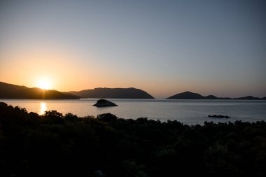 Büyük panoramik dağ manzarası siluetler, deniz ve gökyüzü yükselen güneşle.