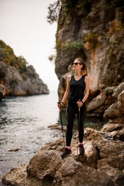 Güzel bir kadın, taşın üzerinde, doğa manzarasının arka planında duruyor.