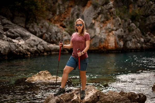 Mulher em óculos de sol em pé contra o pano de fundo borrado de pedras e água do mar — Fotografia de Stock