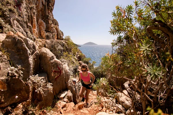 Jonge vrouw met trekking palen in haar handen klimmen op de rotsachtige pad — Stockfoto