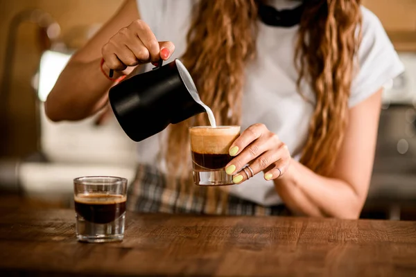 Primer plano en vidrio con bebida de café en el que la mujer barista vierte crema de leche batida — Foto de Stock
