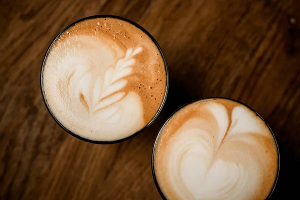 Beyaz köpüklü, ahşap masadaki kahve bardaklarının üst görüntüsü.. — Stok fotoğraf