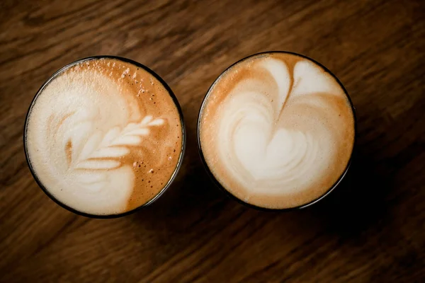 Beyaz köpüklü, ahşap masadaki resim desenli kahve bardaklarının üst görüntüsü.. — Stok fotoğraf