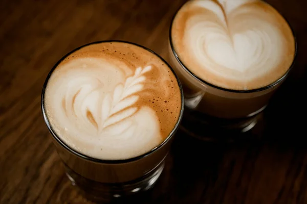 Vue des verres de café avec motif sur mousse blanche sur table en bois. — Photo