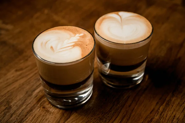 Verres transparents de café avec motif sur mousse blanche sur table en bois. — Photo