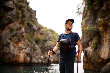 Kayalıkların ve gökyüzünün arka planında duran ve başka yere bakan adam.