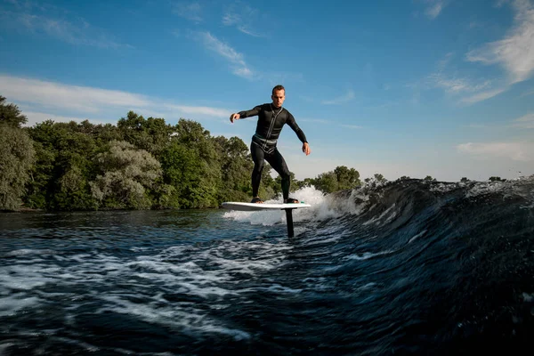 Gesunder Mann balanciert an sonnigem Tag auf Tragflächenfolie auf Welle — Stockfoto