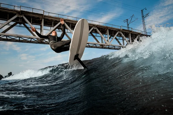 man riding the wave on foilboard on background of bridge and blue sky