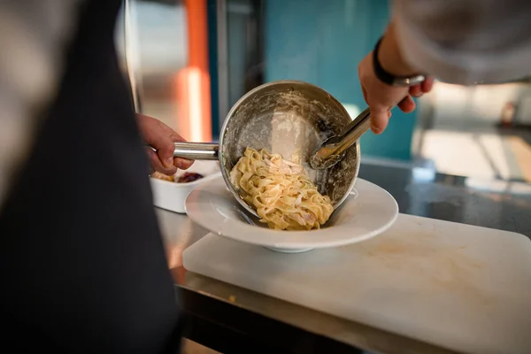 Male chef takes out cooked pasta from pan and puts it in a plate. — Stock Photo, Image