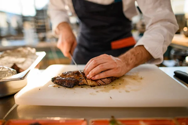 Mannelijke chef snijdt gebakken stuk vlees op snijplank. — Stockfoto