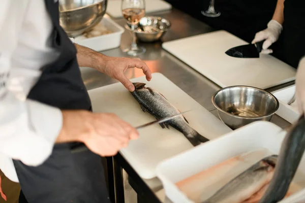 Chef snijdt verse vis op wit bord in de keukentafel. — Stockfoto