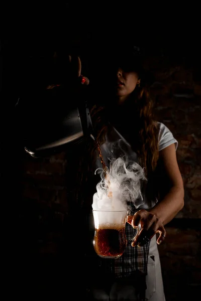 Женщина-бариста наливает горячий напиток из кофейника в прозрачный стакан в руке — стоковое фото