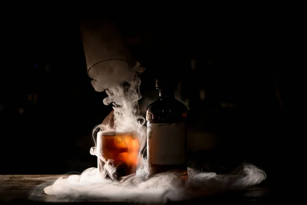 Hermosa copa antigua de cóctel y botella en bar oscuro con maravilloso humo blanco alrededor — Foto de Stock