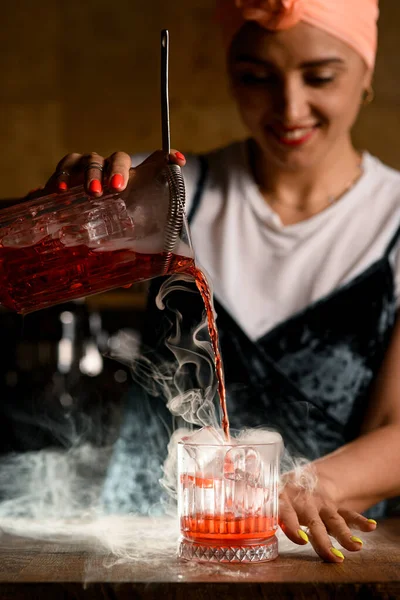 잔을 섞어 증기가 나는 유리에 담근 차가운 음료를 붓는 여자 바텐더 — 스톡 사진