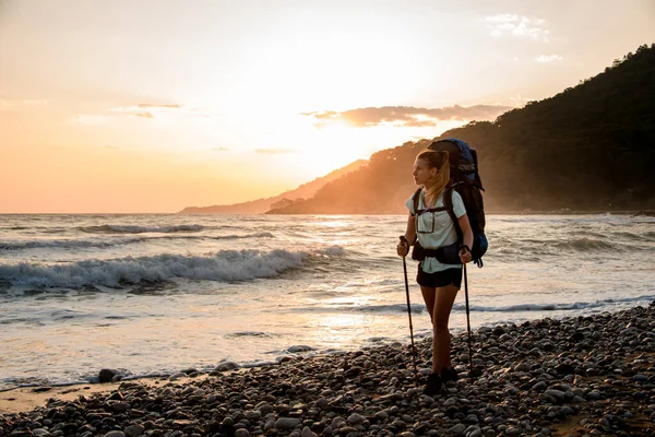 Mujer hermosa turista en la orilla del mar contra el telón de fondo de las montañas y la puesta del sol —  Fotos de Stock