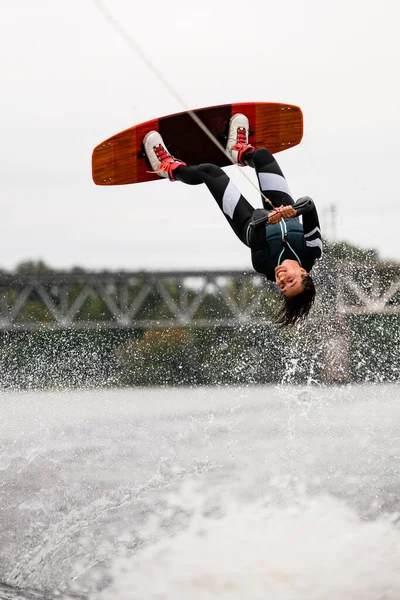 Belle femme wakeboarder tient la corde et faire des flips et sauter par-dessus l'eau sur wakeboard — Photo