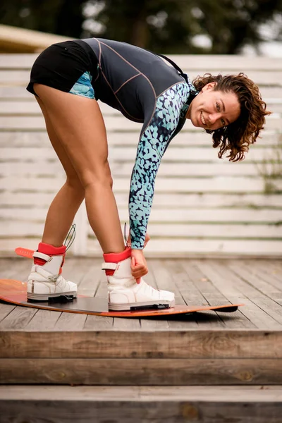 Ung leende kvinna fixa sina ben i stövlar på en wakeboard — Stockfoto
