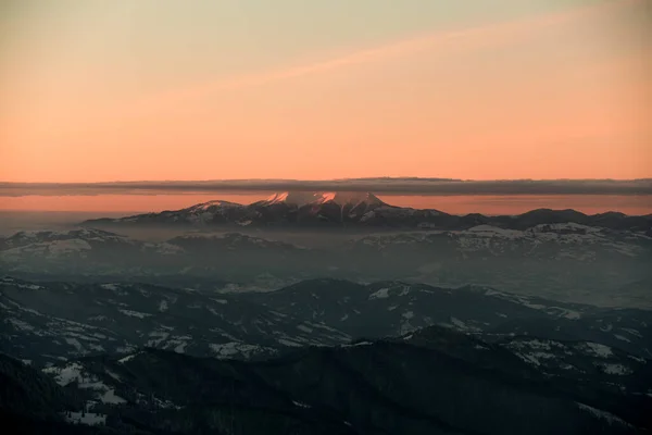 Magnifik utsikt över bergstopp mot bakgrund av ljus orange himmel med moln på toppen — Stockfoto