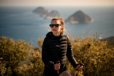 Güneş gözlüklü ve deniz manzaralı yürüyüş direkleri olan yakışıklı bir kadın.