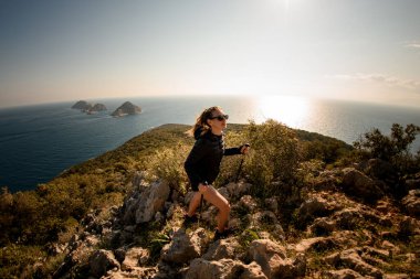 Deniz manzaralı patika boyunca yürüyüş direkleri olan bir kadının panoramik görüntüsü