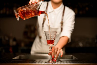 Kadın barmen cam bardakla süzgeci karıştırıp kristal bardağa koyar.