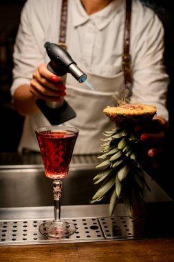 Kadın barmen ananasın tepesini tutar ve üzerine benzin yakar..