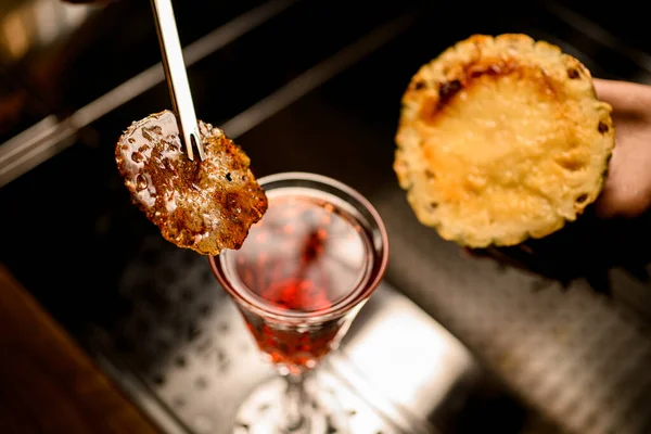 Bovenaanzicht van verbrande karamelkorst in stalen pincet over glas met drank. — Stockfoto