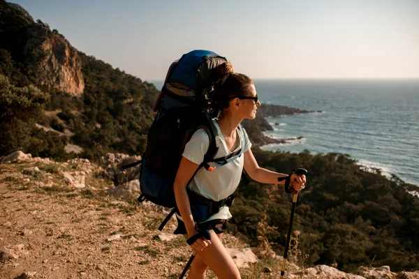 Mujer guapa con mochila y bastones de senderismo caminando sobre el telón de fondo de hermoso paisaje marino —  Fotos de Stock