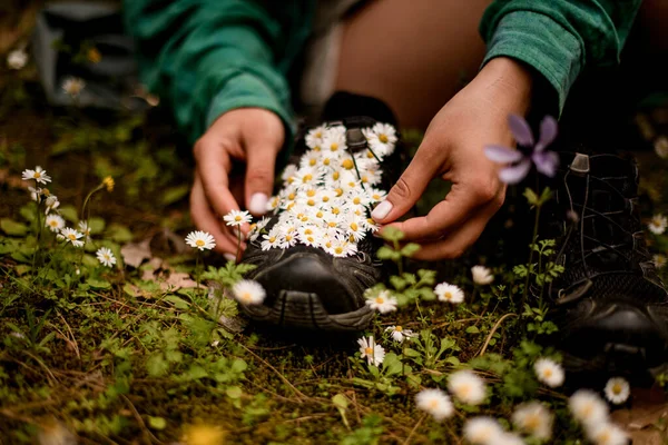 Spor ayakkabılarına papatya çiçeği seren kadının ellerine odaklan.