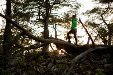 Genç atletik kadın ormandaki ağaçların arkasındaki devrilmiş ağaçta duruyor.