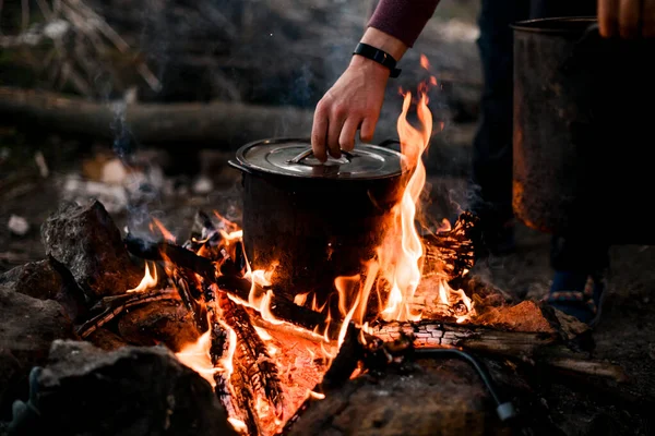 Man hand holds the lid of saucepan that stands on burning fire — стоковое фото