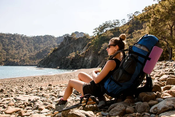 Mujer joven con una gran mochila de senderismo descansando en la costa rocosa — Foto de Stock
