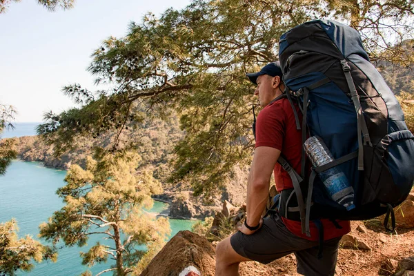 Man vandrare med ryggsäck stå på stigen och tittar mot havet bukten — Stockfoto