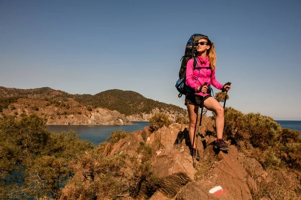 Sportieve vrouw met rugzak en trekking palen staat op steen tegen de achtergrond van het landschap — Stockfoto