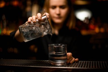 Kadın barmen elinde karıştırıcı bardaklar ve bardakları buzlu ve yaban mersinli eski moda bardaklara doldurur.