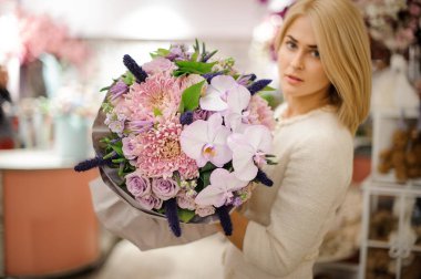 Çekici sarışın kadın güzel bir buket kasımpatı orkide çiçeği ve gül tutuyor.