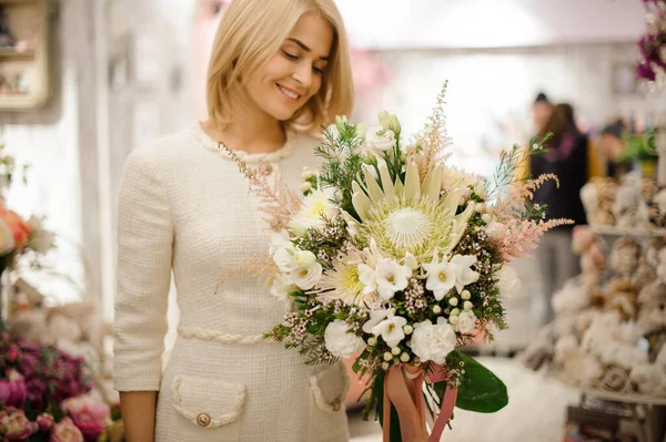 Дивовижний букет з різних білих квітів, прикрашений зеленню в руках блондинки — стокове фото