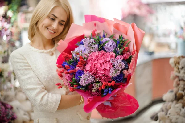 Mujer sonriente sostiene hermoso ramo de flores mixtas envueltas en papel rosa brillante —  Fotos de Stock