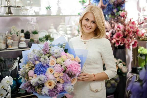 Mujer rubia sonriente con hermoso ramo de varias flores en su mano en la tienda de flores — Foto de Stock