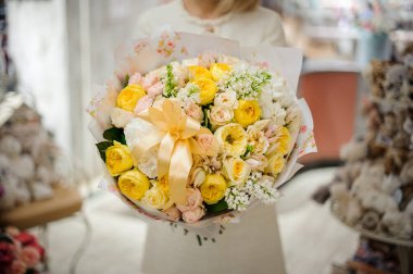 Güzel bir buket beyaz bej ve sarı güller kağıda sarılıp kadın eli kurdelesiyle süslenmiş.